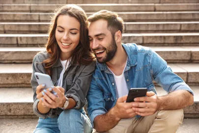 Junges Paar sitzt auf einer Treppe und schaut gemeinsam auf Smartphones