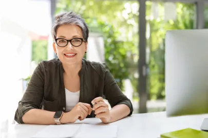 Frau mit Brille sitzt lächelnd an einem Schreibtisch
