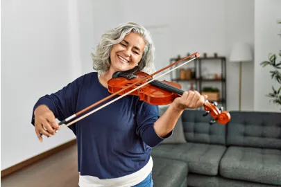 Frau spielt lächelnd Geige in einem Wohnzimmer